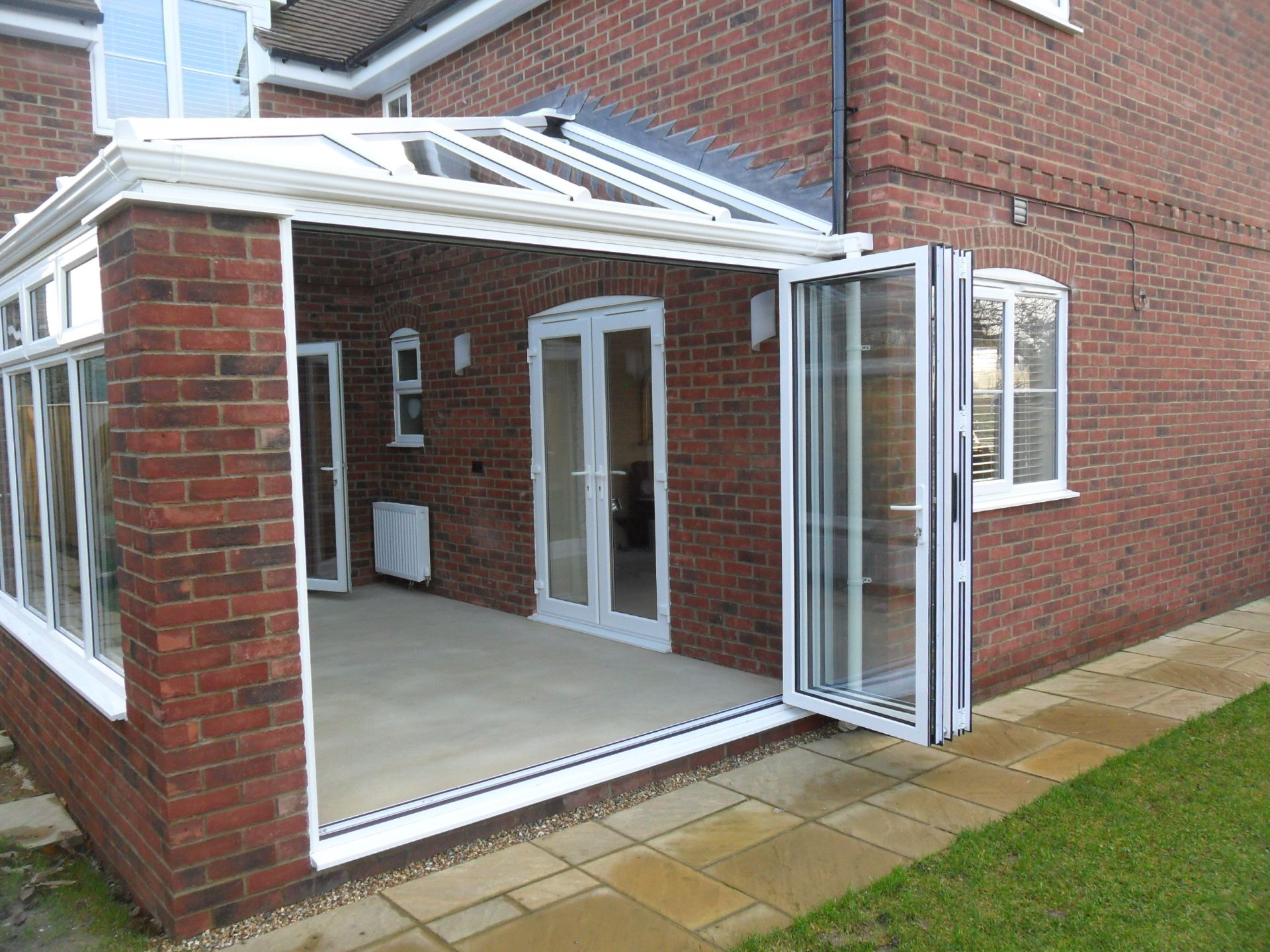 White bi-fold doors folded open on the corner of a brick garden room